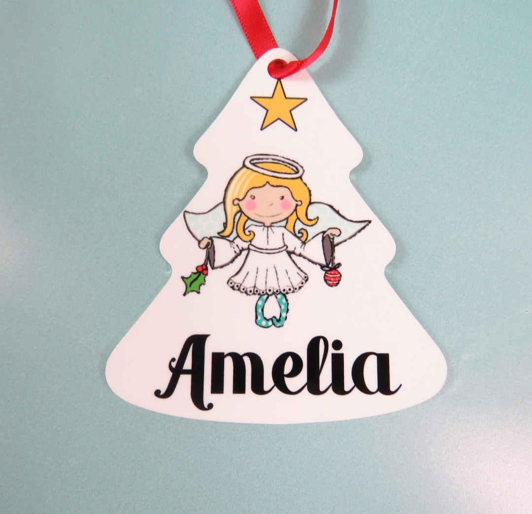 A metal tree-shaped bauble featuring a hand-drawn angel with a personalised name. The decoration is hanging by a ribbon on a Christmas tree branch.