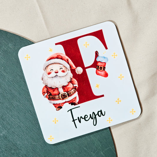 A personalised Christmas coaster featuring a large initial with Santa standing next to it and a custom name beneath. Perfect for festive drinks and holiday décor.

