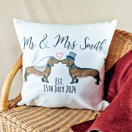 Personalised 40x40cm cushion cover featuring two dachshunds in wedding attire. One dog wears a veil and the other a top hat and dicky bow. Custom text options include 'Mr & Mrs [Name]', 'Mr & Mr', or 'Mrs & Mrs' with the wedding date below. Canvas feel with zip closure at the bottom.