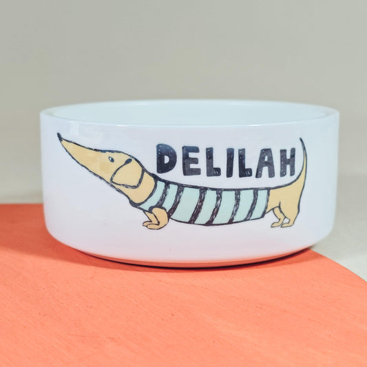 Personalised dachshund dog bowl featuring a sausage dog in a stripey jumper, with the dog's name on the bowl. Available in three sizes, perfect for any dachshund lover.