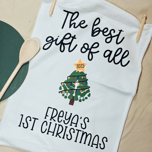 Personalised Christmas tea towel featuring a baby’s green footprint shaped like a Christmas tree, reading “The Best Gift of All – [Name]’s 1st Christmas [Year]”.