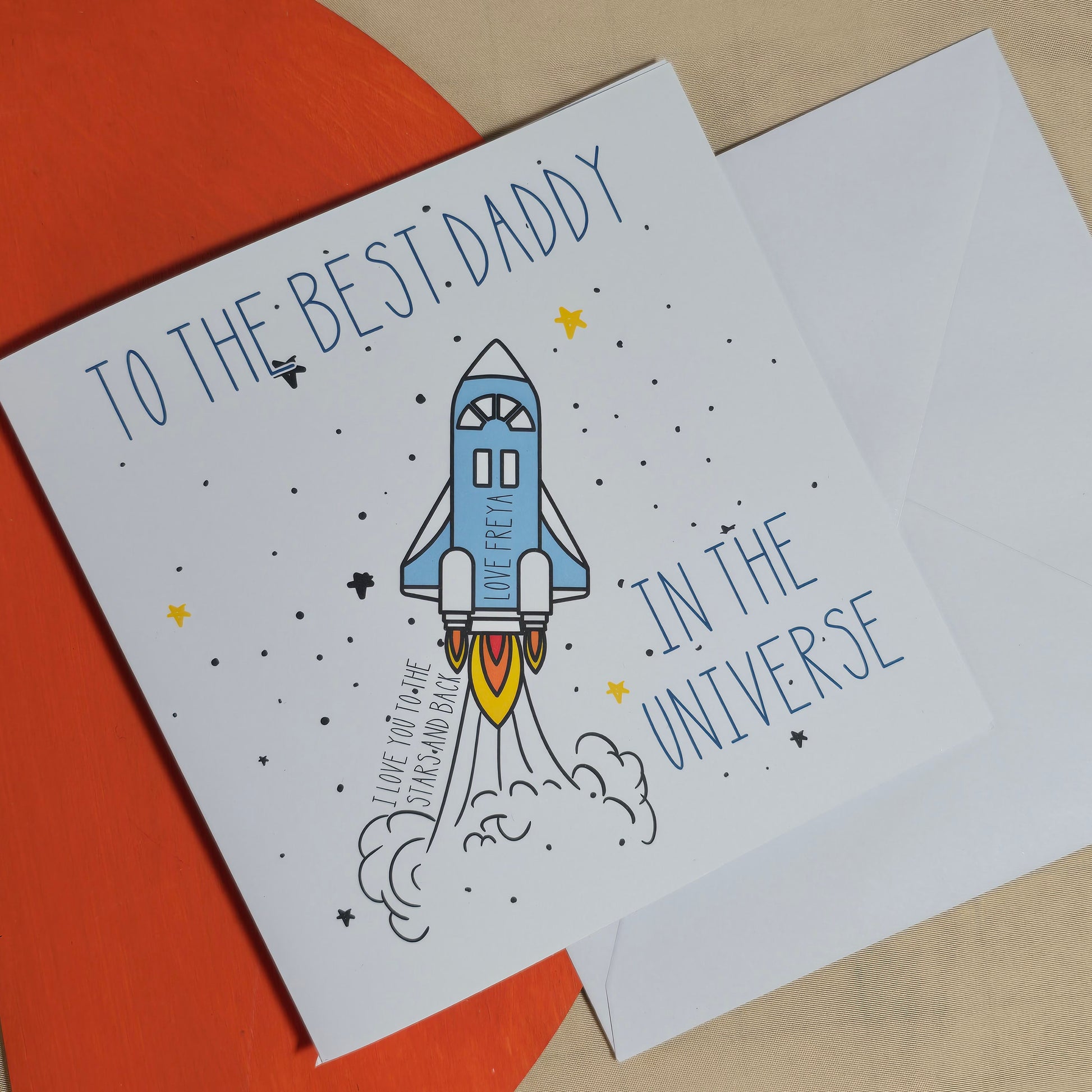 Greeting card with a rocket illustration and text for the best daddy in the universe on an orange and beige background.