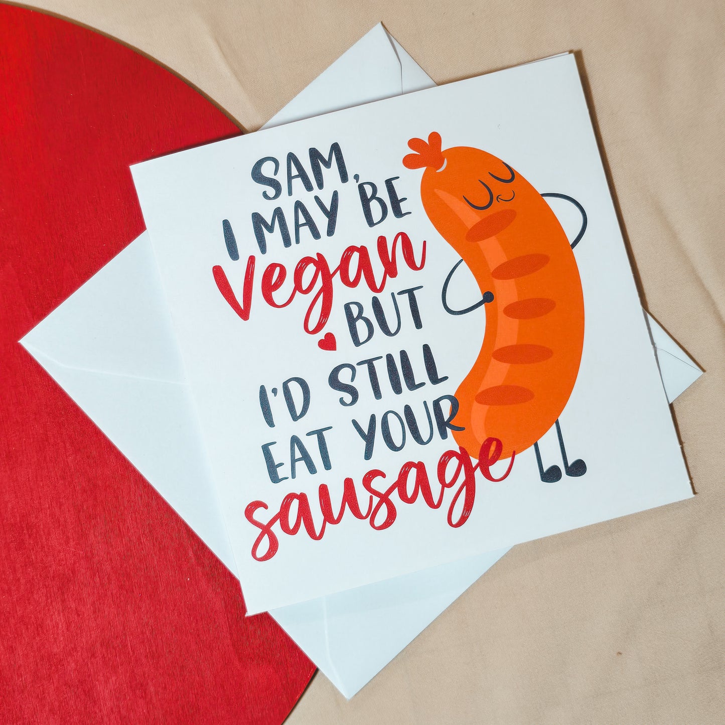 Funny vegan Valentine’s card with the text "[Name], I may be vegan, but I’d still eat your sausage" in a playful font, featuring a cheeky design. Square card with personalisation options, paired with a white envelope.