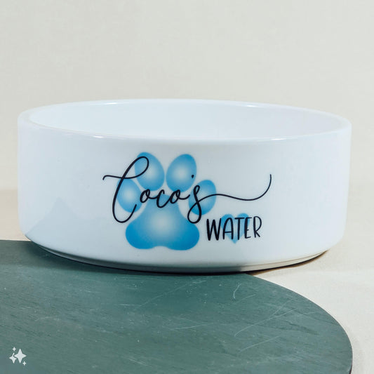 A white pet bowl with a blue paw print design, personalised with "Name's Water" or "Name's Food." The colour can be customised, and it comes in three sizes. Perfect for any pet!