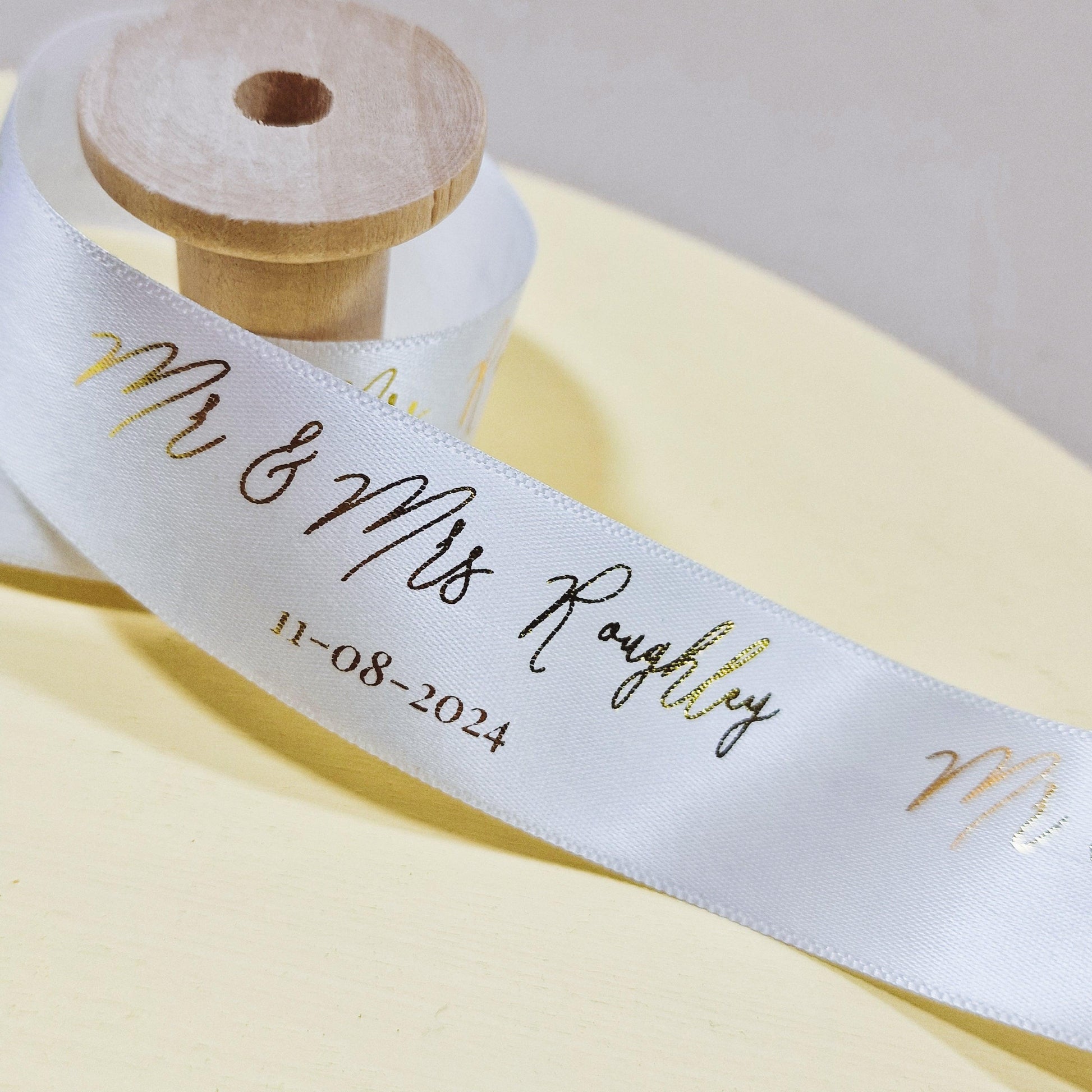 Custom wedding ribbon printed with "Mr & Mrs [Name]" and wedding date. 25mm wide, available in various colours, with options for "Mr & Mr," "Mrs & Mrs," and other titles.