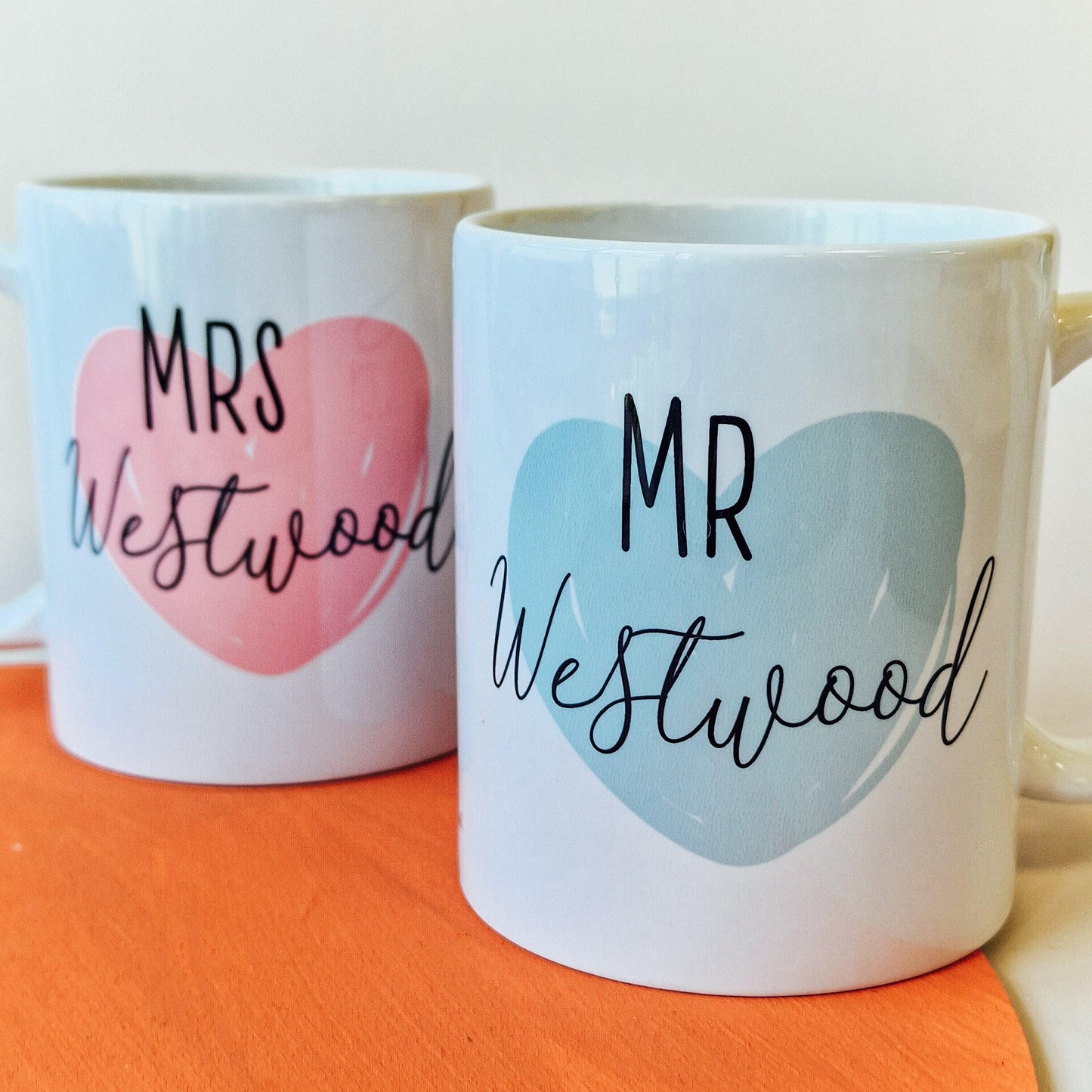 Pair of personalised mugs, one saying "Wifey" with a pink heart and wedding date, and the other saying "Hubby" with a blue heart and wedding date. Custom names on the back. Available in 10oz and 15oz sizes, dishwasher safe.